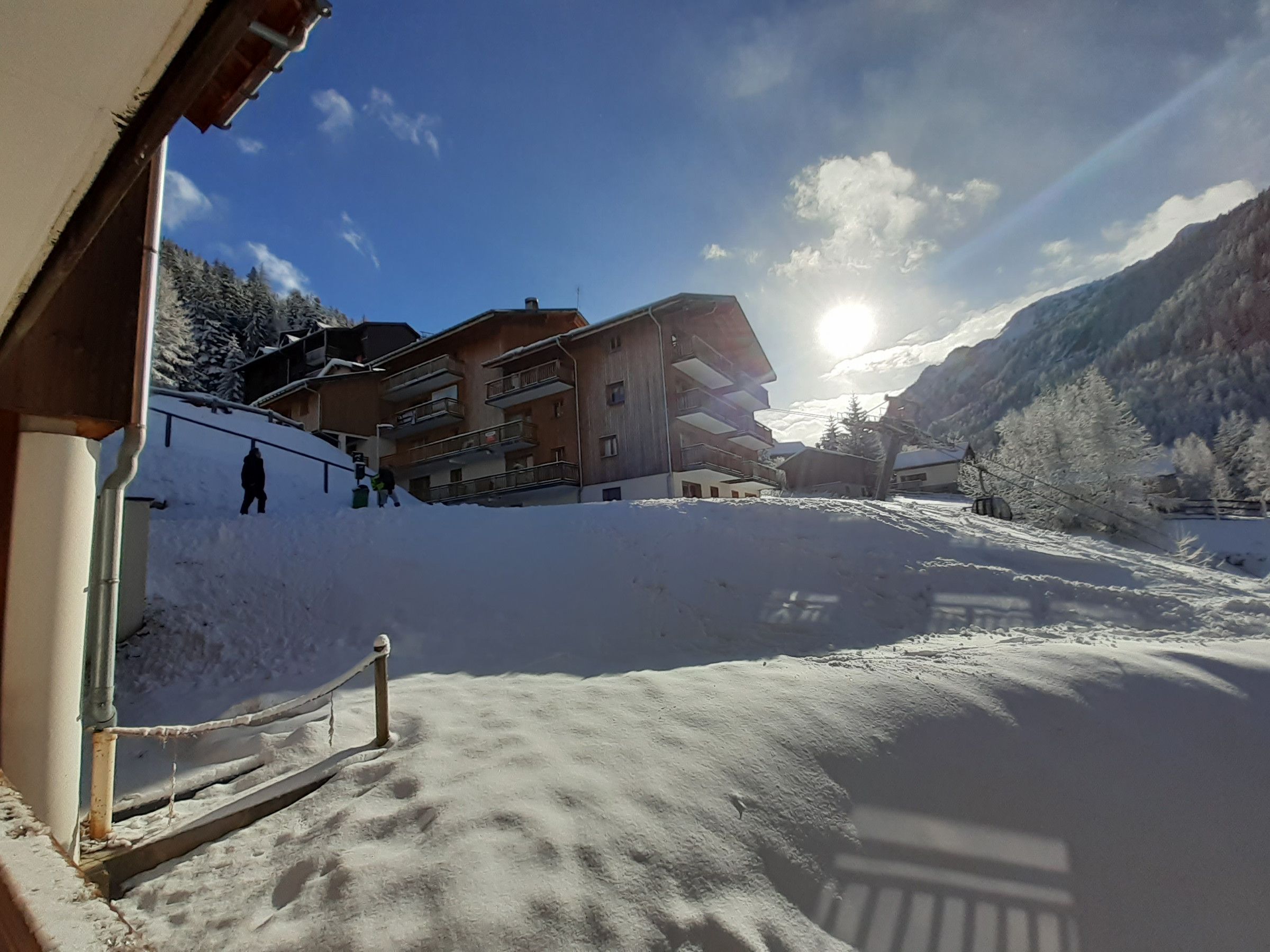 A snow-covered mountain slope with a building and a person in the distance.