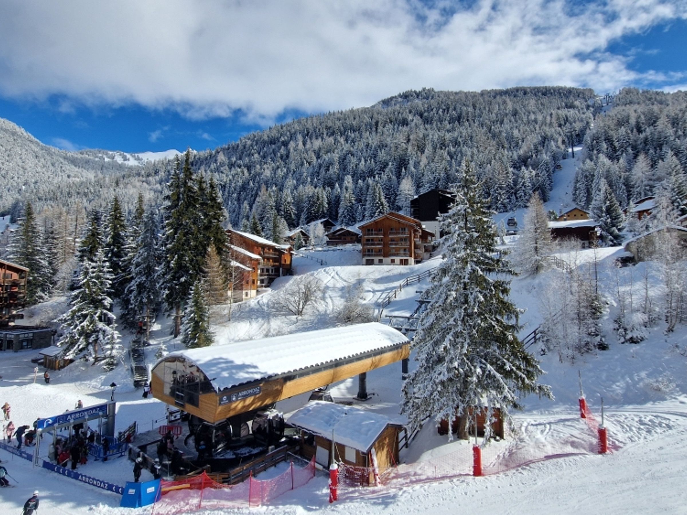 A snow-covered mountain resort with multiple wooden buildings, ski lifts, and a clear sky.