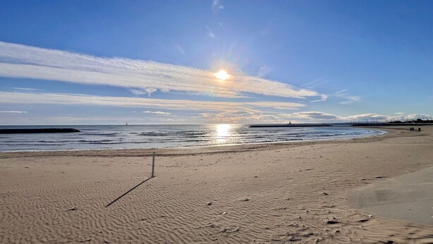 Ein Strand mit blauem Himmel und der untergehenden Sonne am Horizont.