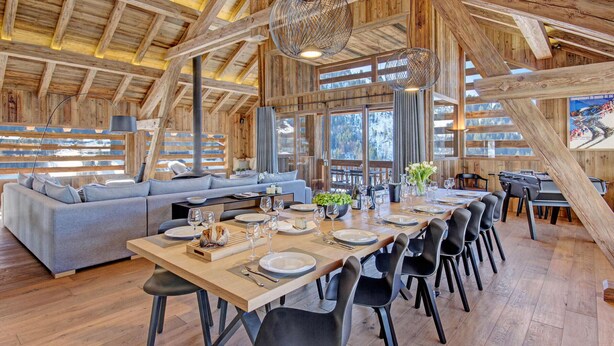 Un vaste espace dédié à la salle à manger, avec une longue table en bois dressée pour le repas, entourée de chaises modernes.