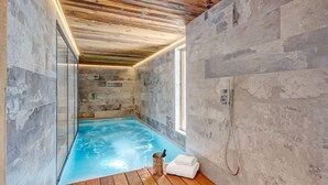 Une piscine intérieure moderne dotée d’un plancher en bois, de murs en pierre et d’une structure en verre.