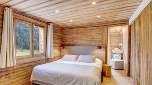 Une chambre à coucher dans une cabane en bois, avec un lit, une table de chevet, une lampe et une vue sur la forêt par la fenêtre.