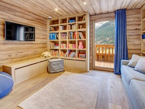 Een gezellig cabinteinterieur met een houten boekenkast, een televisie, een bank en uitzicht op een bebost berglandschap.