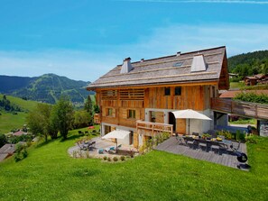 A wooden chalet with a deck, outdoor seating, and a scenic mountain backdrop. - 5★ chalet, 15 people, indoor pool, mountain views, 7 bedrooms, terrace, pets welcome (La Clusaz)