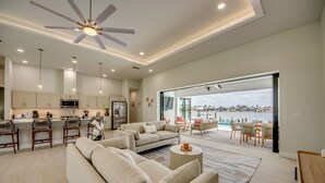 Una sala de estar moderna con un sofá grande, una mesa de centro y vistas a una piscina y al horizonte urbano a través de amplios ventanales.