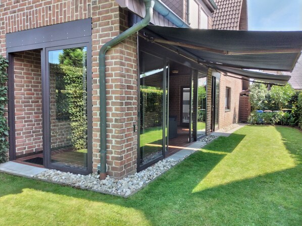 Une maison moderne avec une façade en briques, de grandes portes vitrées et un espace extérieur couvert.