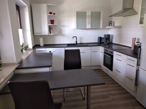 Une cuisine moderne avec des meubles blancs, un plan de travail noir, un four encastré et un coin repas comprenant une table et des chaises.