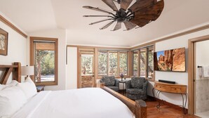 Ein geräumiges Schlafzimmer mit einem großen Bett, einem Deckenventilator, einem Schreibtisch mit Stuhl und einem großen Fenster mit Blick ins Freie.