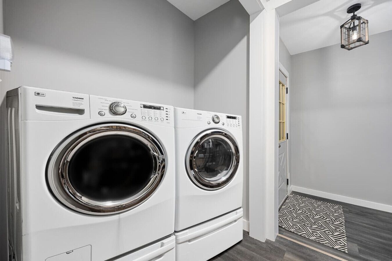 A laundry room with two front-loading washing machines, a patterned rug, and a hanging light fixture.