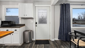 A compact kitchen with white cabinets, a microwave, a trash can, and a door with a frosted glass panel.