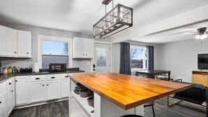 A modern kitchen with white cabinets, a wooden island, a microwave, and a ceiling fan.