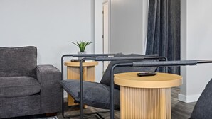 A modern living room with a grey sofa, a small round wooden table with a plant, and a black metal frame structure.