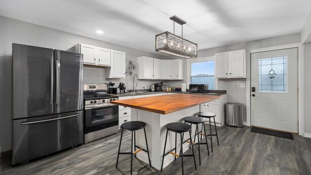 A modern kitchen with stainless steel appliances, a wooden island with bar stools, and a view of the sea through a glass door.