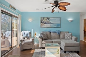 A living room with a ceiling fan, a sofa, a coffee table, and a painting of a beach scene.