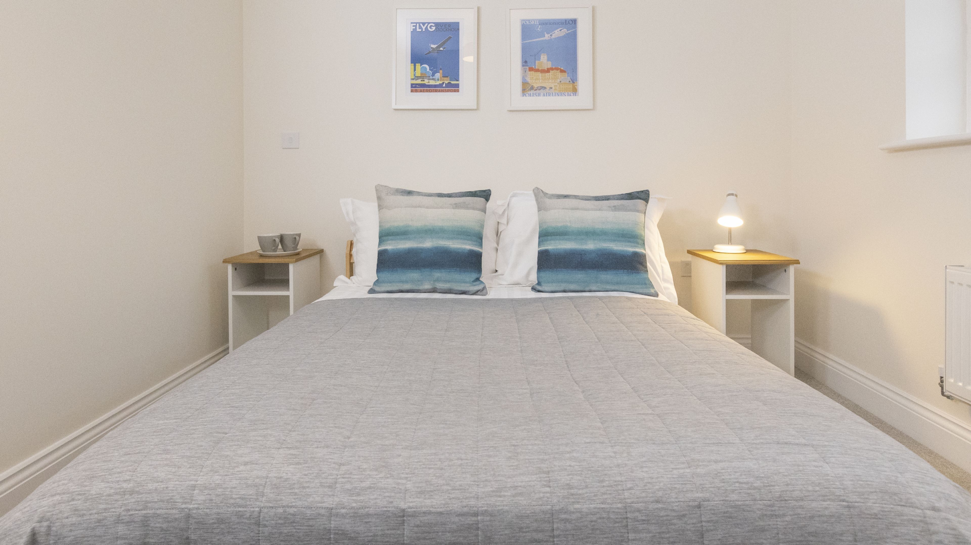 Ein Schlafzimmer mit einem Bett, zwei Nachttischen, einer Lampe und zwei gerahmten Bildern an der Wand.