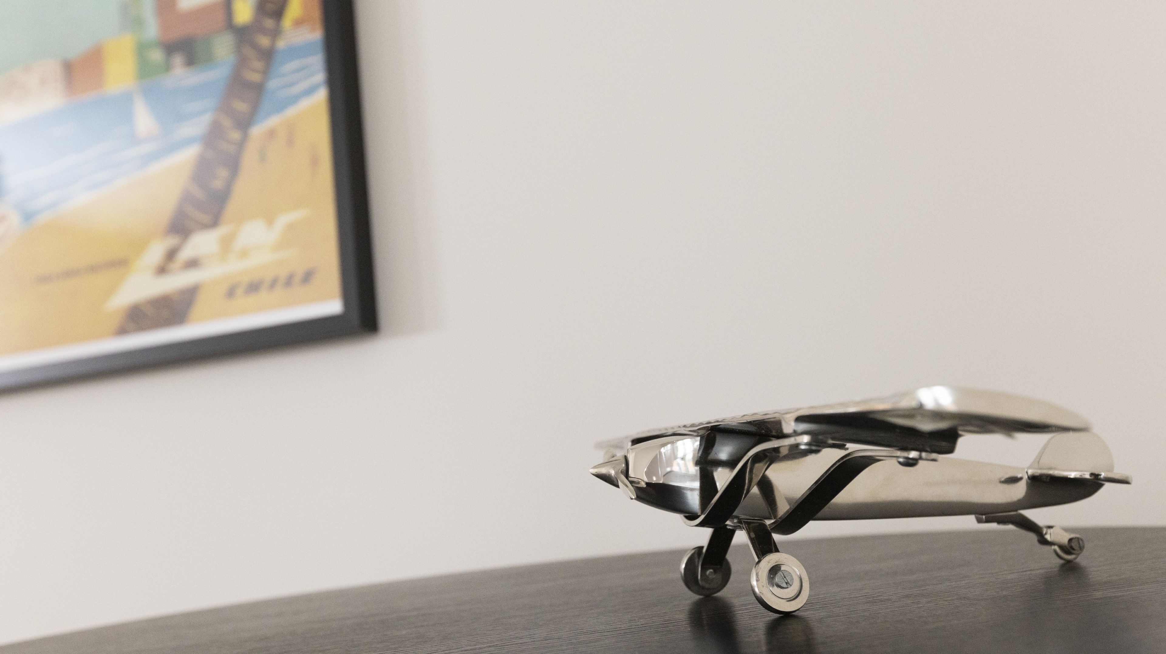 A small, metallic airplane model on a table with a framed picture in the background.