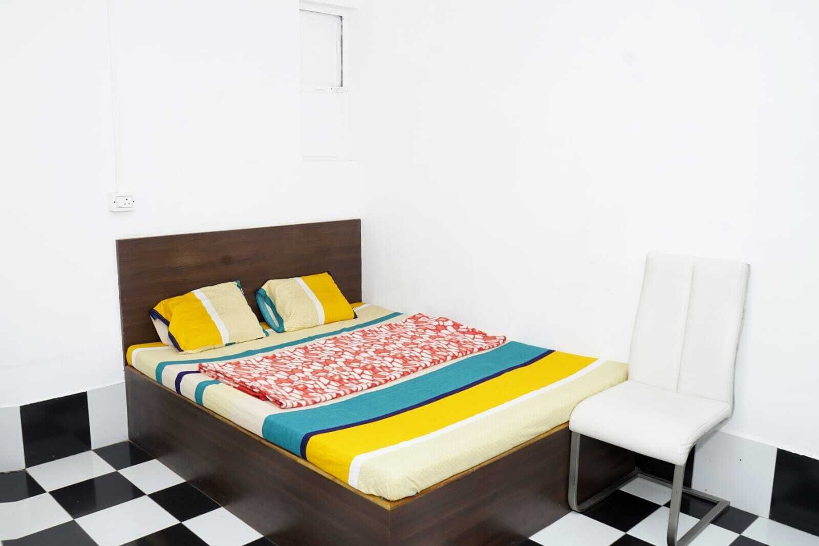 A bed with a wooden headboard, a white chair, and a checkered floor.