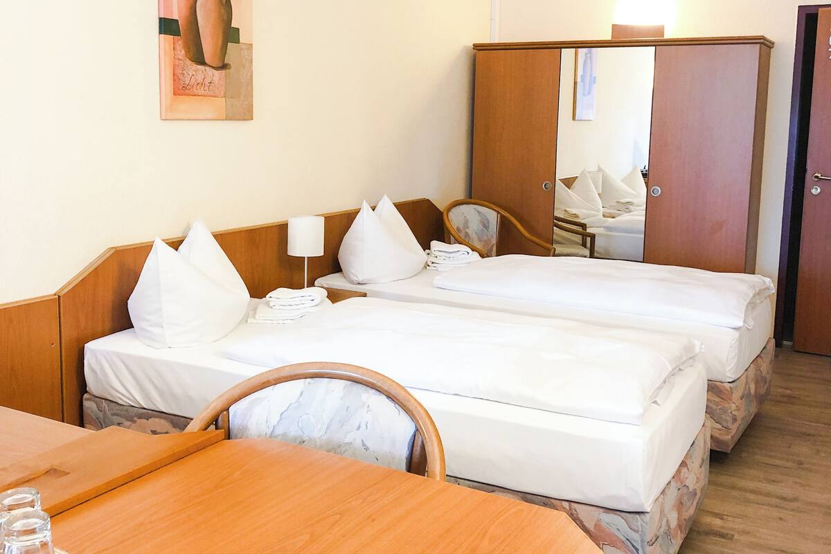 A hotel room with two beds, a wooden table, a chair, a mirror, and a painting on the wall.