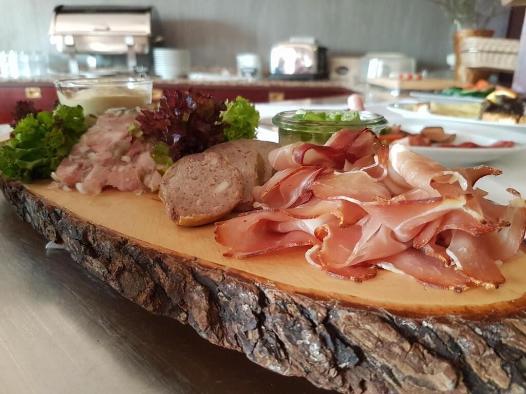 A wooden board with various meats and vegetables, likely part of a buffet or food station.
