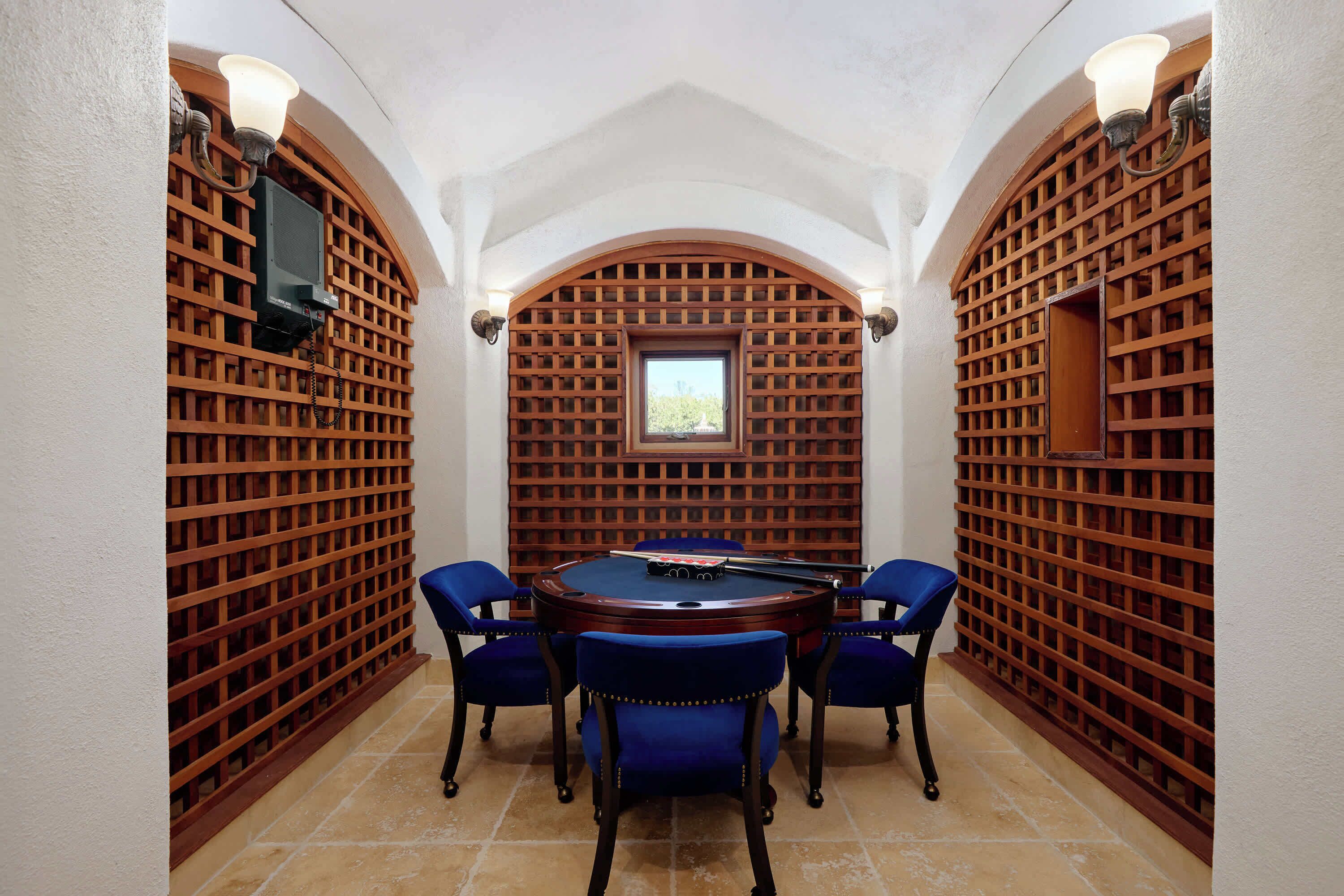 A billiards room with a pool table, four blue chairs, and wooden lattice walls.