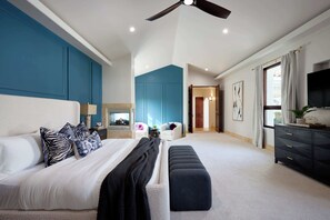 A modern bedroom with a large bed, a bench, a TV, and a ceiling fan. - Entertainers Paradise! $6M Estate with Lagoon Pool (Paradise Valley)