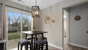 Un espace repas comprenant une table et quatre tabourets, un luminaire suspendu et des éléments de décoration murale.