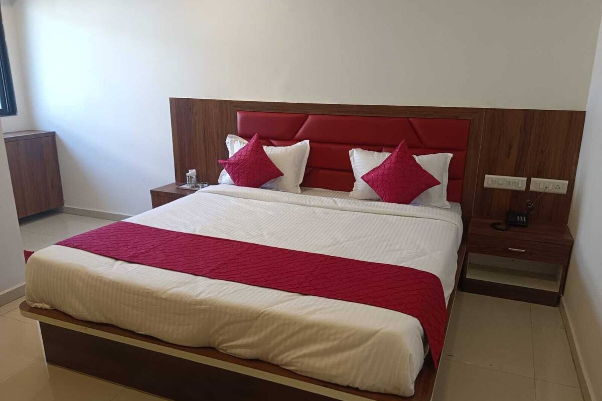 Un lit bien fait, recouvert d’une couvre-lit rouge et blanche, avec une tête de lit en bois et deux tables de chevet dotées de lampes.
