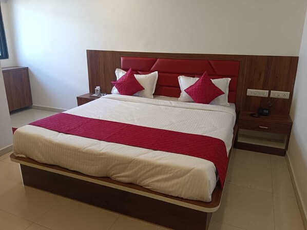 A neatly made bed with a red and white bedspread, a wooden headboard, and two bedside tables with lamps. - Hotel Govindam Palace (Ahmedabad)