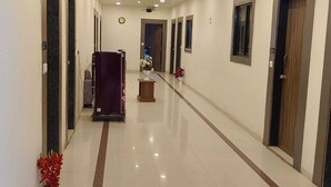 Un corridoio d'hotel dal lungo sviluppo lineare, con diverse porte e un'area centrale caratterizzata da un tavolino e fiori.