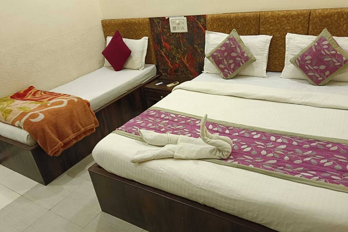 Une chambre d’hôtel avec deux lits simples et un lit plus grand. Chaque lit est équipé d’un oreiller et d’une couverture.