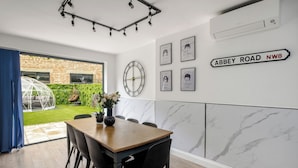 A modern dining area with a wooden table, black chairs, a large wall clock, and framed artwork. - LONDONERS│Fabulous Four Residence  (London)