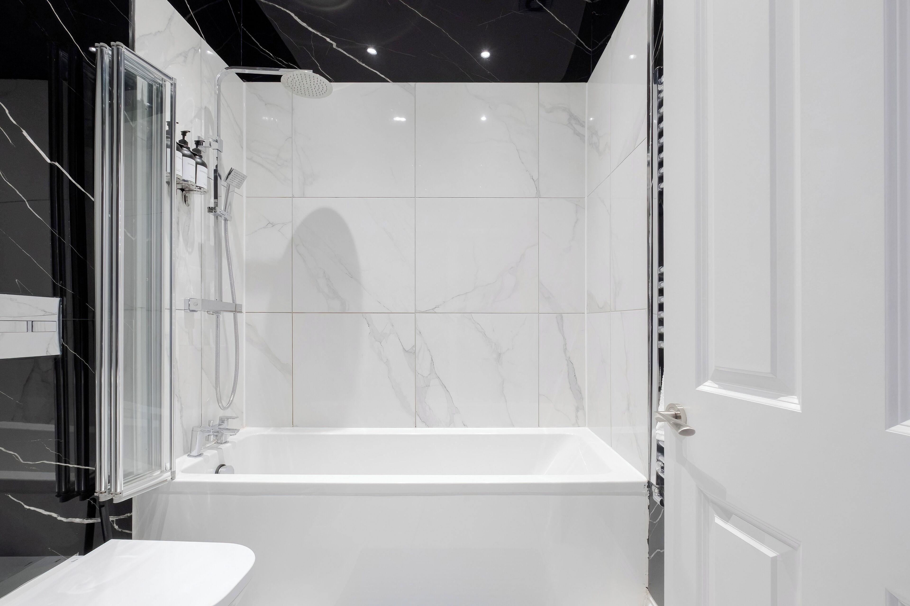 Un baño moderno con ducha de vidrio, bañera blanca y azulejos de mármol.
