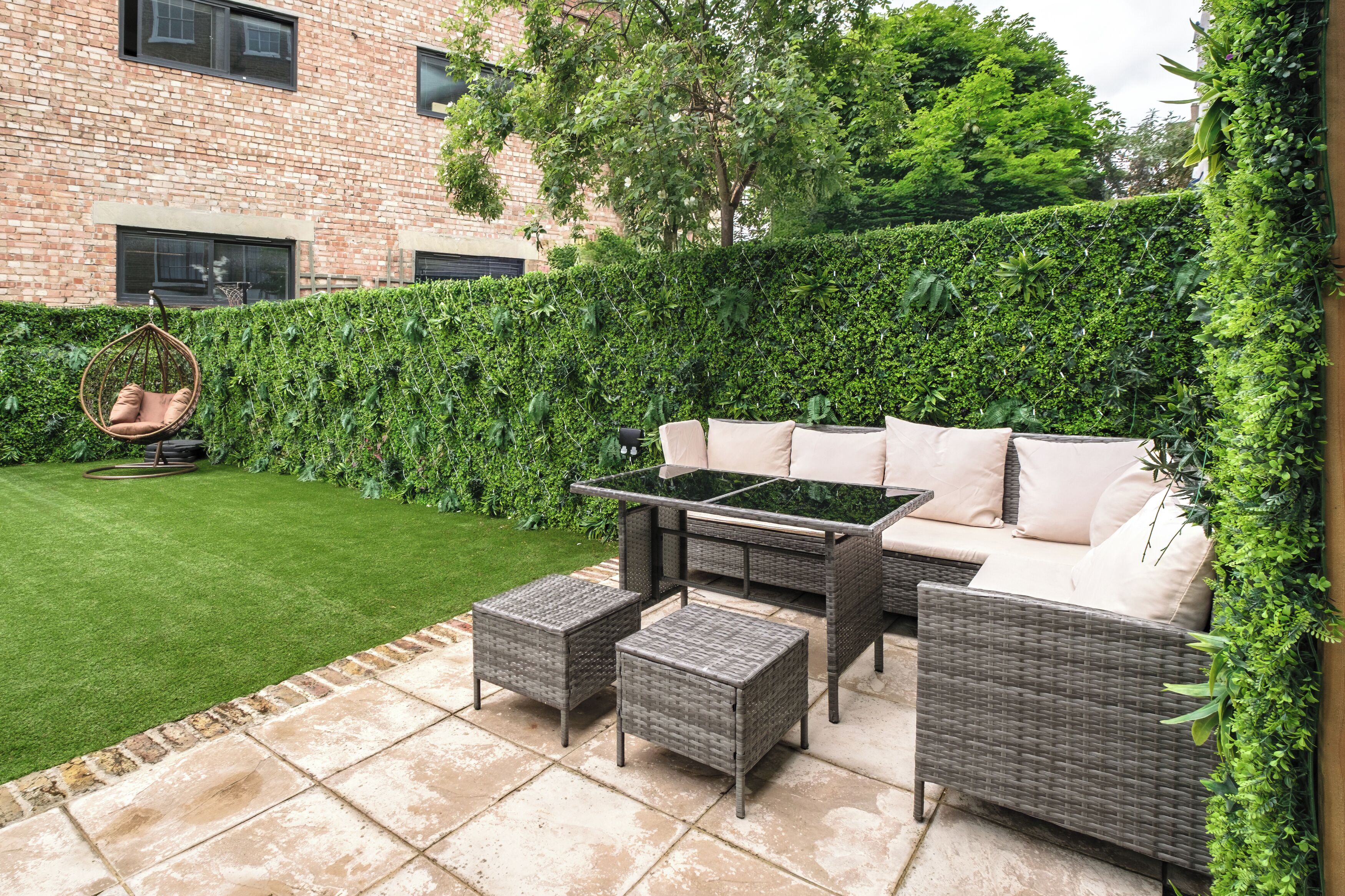 Un patio con muebles de mimbre, una silla colgante y un seto.