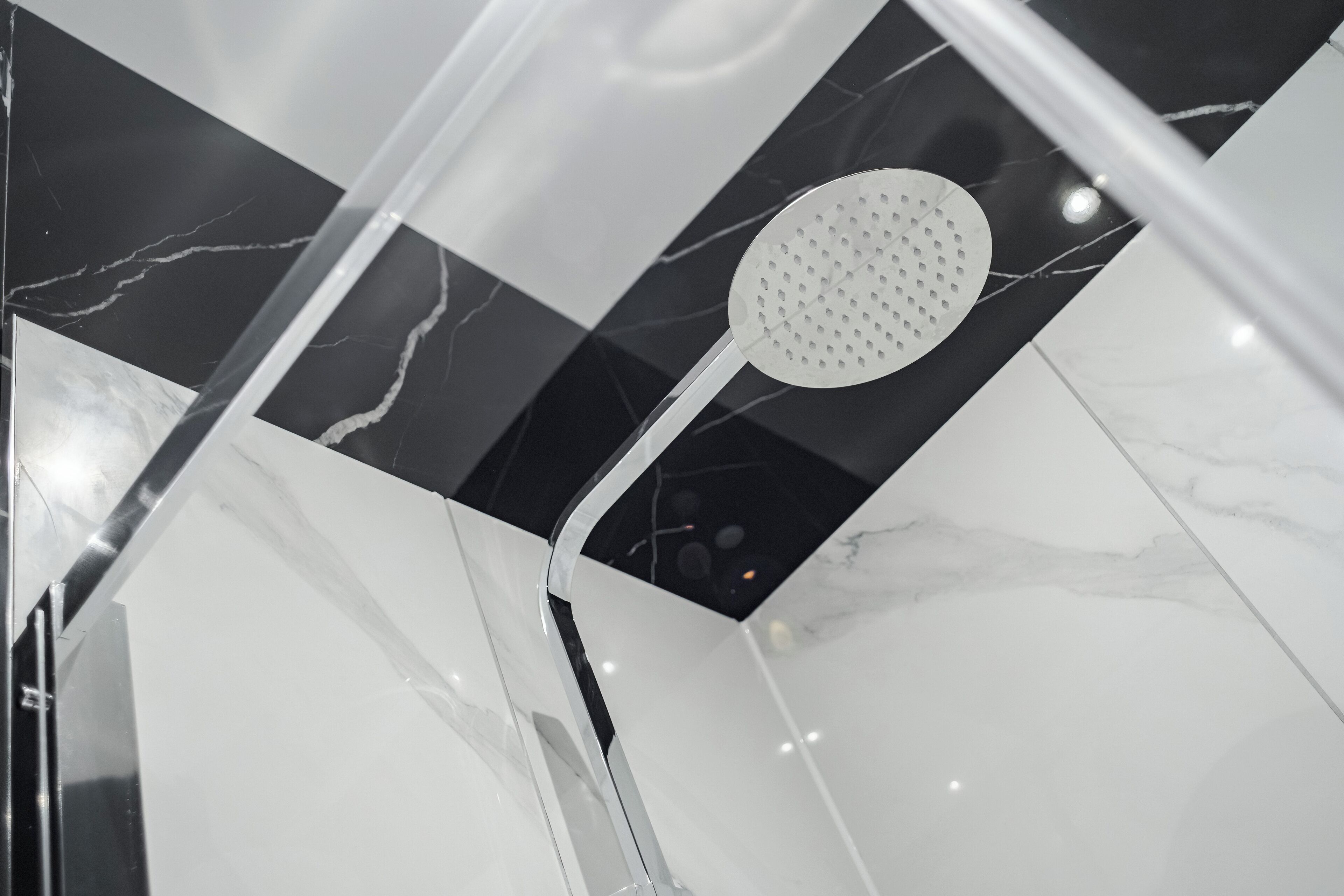 Une douche moderne dotée d’un pommeau de douche perforé, installée sur un sol en marbre noir et blanc.