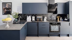 A modern kitchen with dark cabinetry, a built-in oven, and a coffee maker. - LONDONERS│Fabulous Four Residence  (London)