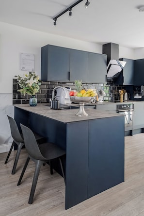A modern kitchen with a central island, dark cabinetry, and a backsplash. - LONDONERS│Fabulous Four Residence  (London)