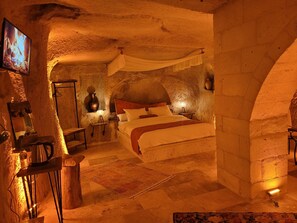 A rustic stone room with a bed, a television, and a table with a kettle. - LA DİAS CAVE CAPPADOCİA (Nevsehir)