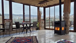 A spacious room with a large window, a stone fireplace, and a patterned rug. - LA DİAS CAVE CAPPADOCİA (Nevsehir)