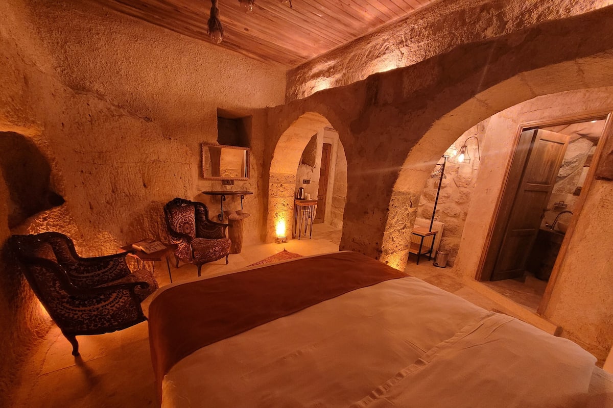 A rustic stone room with a bed, a chair, and a small table.