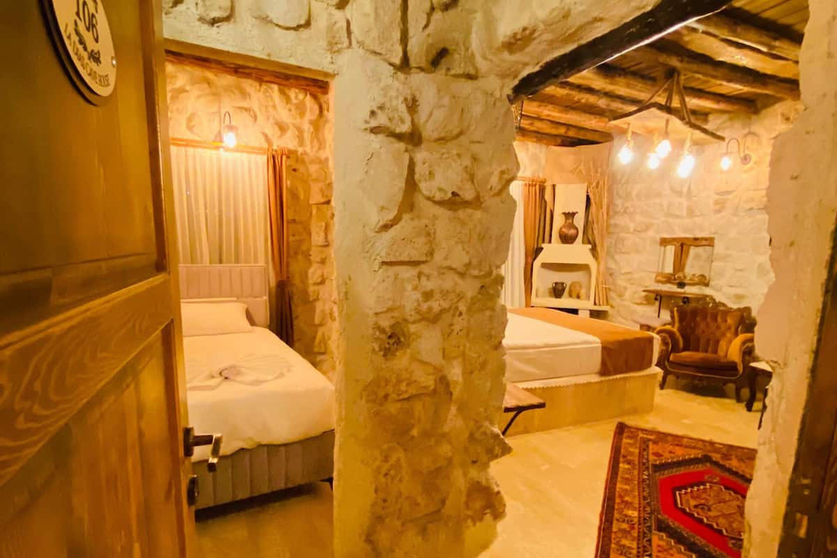 A rustic room with a stone wall, a bed, a wooden cabinet, and a small table with a vase.