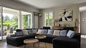 Uma sala de estar moderna com um sofá seccional, uma mesa de centro e uma janela grande com vista para o verde.