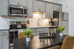 A modern kitchen with stainless steel appliances, a dark countertop, and two potted plants.