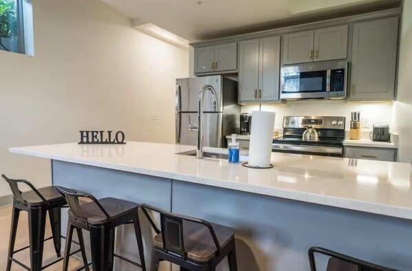 A modern kitchen with grey cabinets, a white island, and a 'HELLO' sign.
