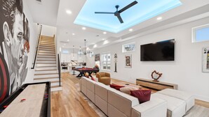 A spacious living room with a ceiling fan, a billiards table, and a large TV. - Modern and sleek unit near Downtown with billiards (Nashville)