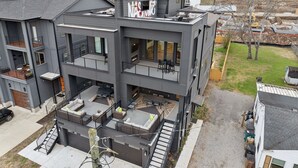 A modern multi-story building with balconies, a rooftop deck, and a visible fire pit area. - Modern and sleek unit near Downtown with billiards (Nashville)