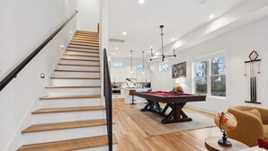 A modern living room with a wooden staircase, a pool table, and a globe on a side table. - Modern and sleek unit near Downtown with billiards (Nashville)