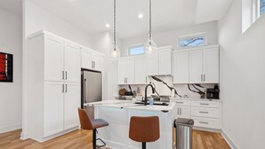 A modern kitchen with white cabinetry, a central island with stools, a stainless steel refrigerator, and pendant lighting. - Modern and sleek unit near Downtown with billiards (Nashville)