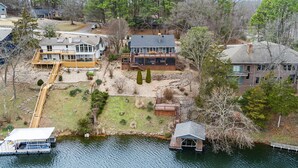 A lakeside property with a dock, a boat, and a large house with a deck and outdoor seating area.