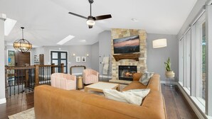 A spacious living room with a stone fireplace, leather sofa, and a dining area with a railing.