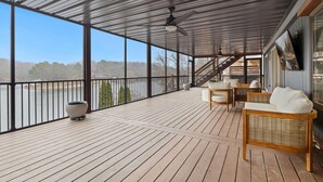 A covered outdoor deck with wooden flooring, a ceiling fan, and a view of a river.